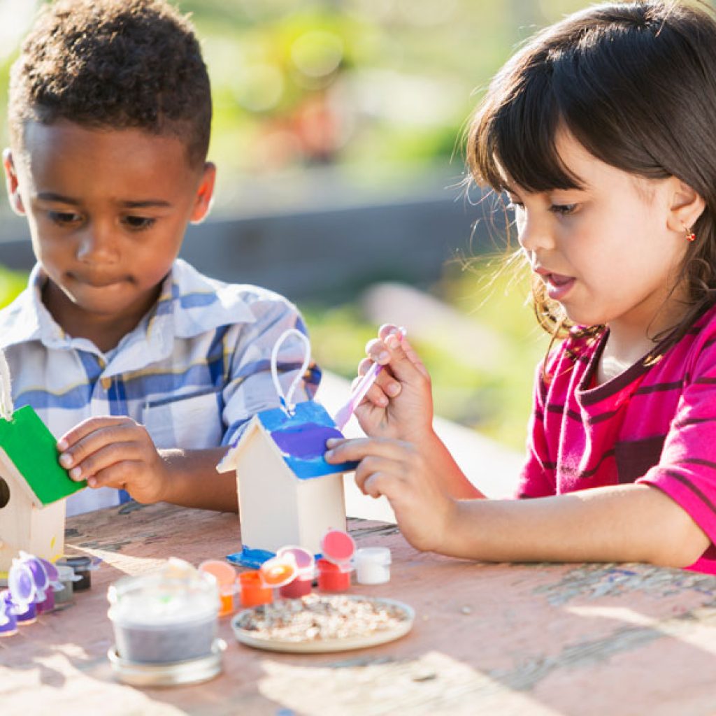 Two children painting wooden birdhouses at a Discovery Corner Academy Summer Camp